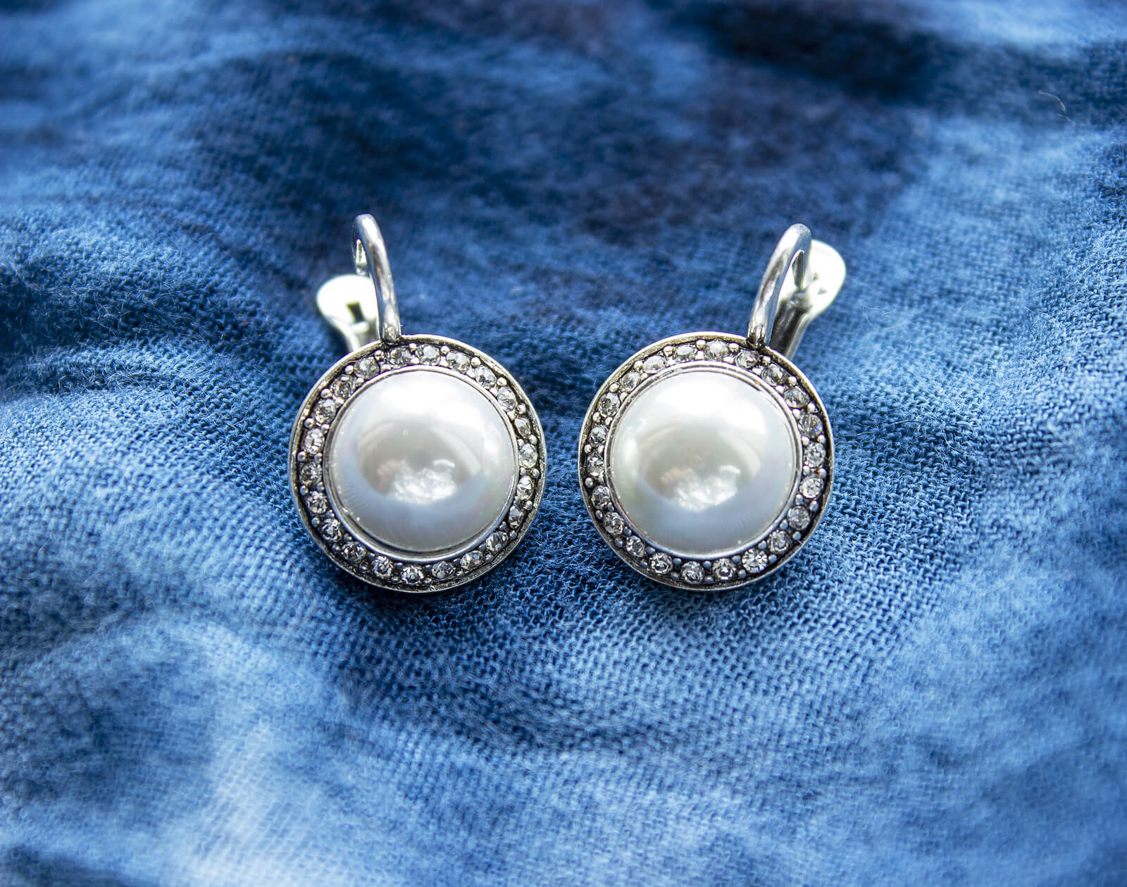 A pair of pearl earrings on a blue cloth.